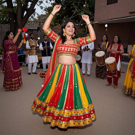 Photograph of a joyful Indian woman in a vibrant red, green, and yellow traditional lehenga, dancing with arms raised, surrounded by musicians and other