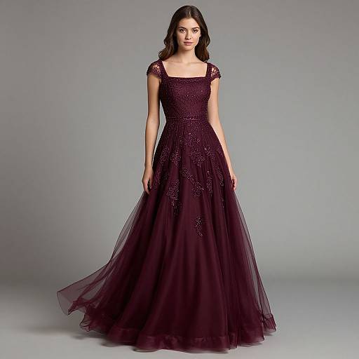 Photograph of a young woman with dark hair wearing a floor-length, deep purple, sheer lace gown with cap sleeves, standing against a gray backdrop.