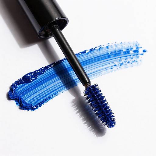 Photograph of a black mascara wand with vibrant blue mascara applied in a thick, brushstroke-like pattern on a white background.