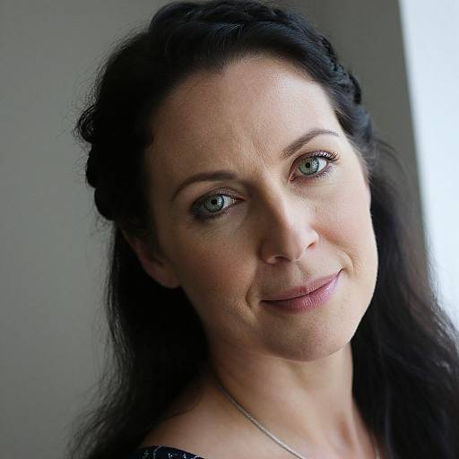 Close-up photograph of a smiling woman with fair skin, green eyes, and long black hair, styled with a braid, wearing a black top.