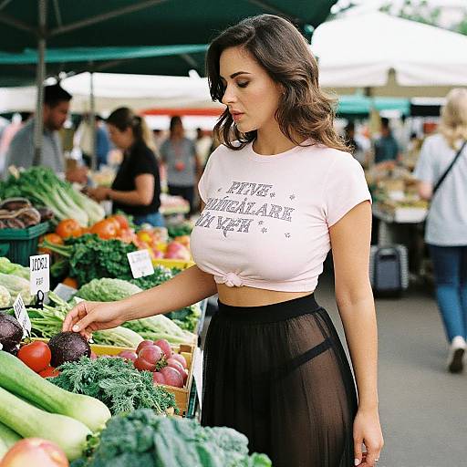 Photograph of a young woman with wavy brown hair, wearing a white crop top and black sheer skirt, shopping at a vibrant outdoor market, selecting