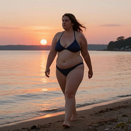 Photograph of a plus-sized woman with dark hair in a black bikini walking along a beach at sunset, with the sun casting a warm orange glow over
