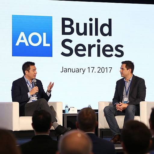 Photograph of two men in suits, seated on chairs, discussing at 