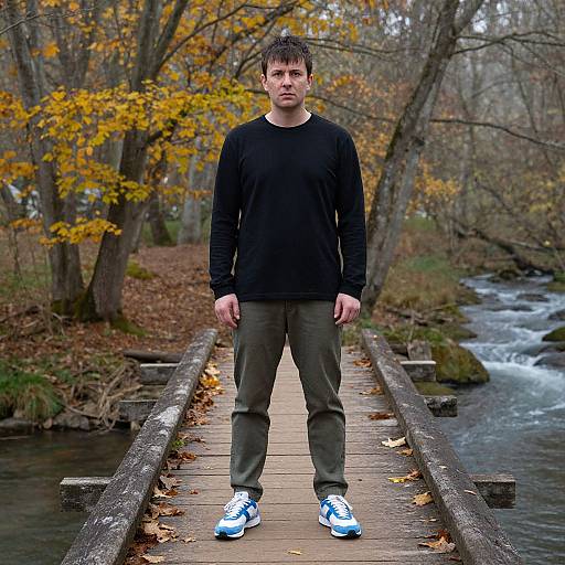 Photograph of a Caucasian man with short brown hair, wearing a black long-sleeve shirt, olive pants, and blue-white sneakers, standing on