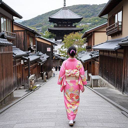 Photograph of a woman in a pink floral kimono walking down a traditional Japanese street with wooden buildings, leading to a pagoda in the background.