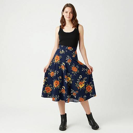 Photograph of a young woman with wavy brown hair, wearing a black tank top and a navy floral skirt, black ankle boots, against a plain