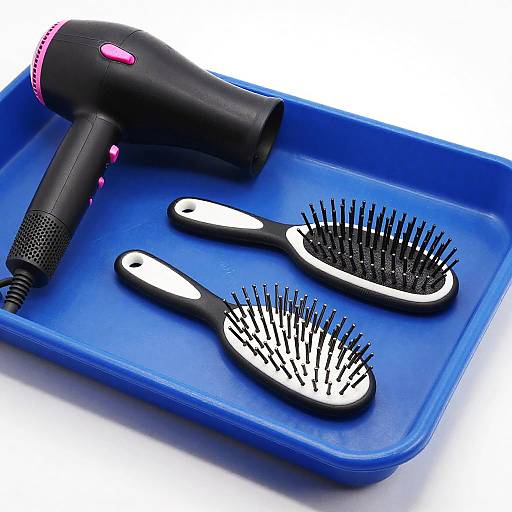 Photograph of a black hairdryer with pink accents, two black and white hairbrushes, on a blue plastic tray.