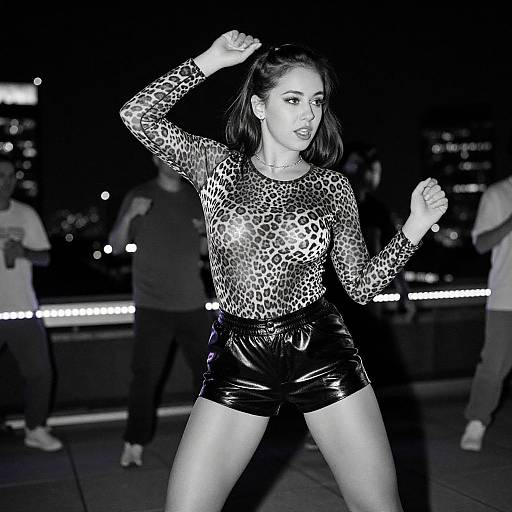 Black-and-white photograph of a woman in a leopard-print top and shiny black shorts, boxing in a dimly lit urban rooftop setting, with blurred background