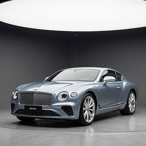 Photograph of a sleek, silver Rolls-Royce Wraith luxury coupe with polished chrome wheels, displayed under a curved, brightly lit ceiling in a