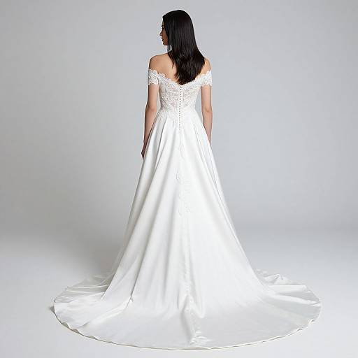 Photograph of a woman with long black hair, wearing an off-shoulder, white lace and satin wedding gown with a long train, standing against
