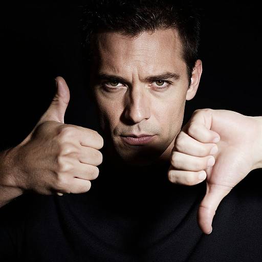 Photograph of a serious, dark-haired man with pale skin, giving two thumbs up against a black background, illuminated from below.