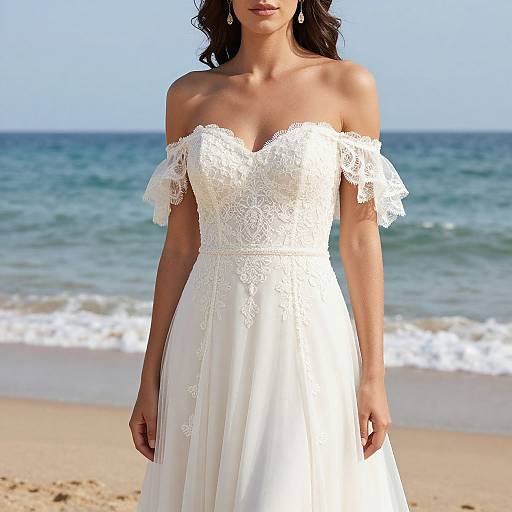 Photograph of a woman with wavy dark hair, wearing an off-shoulder white lace wedding dress, standing on a sandy beach with blue ocean