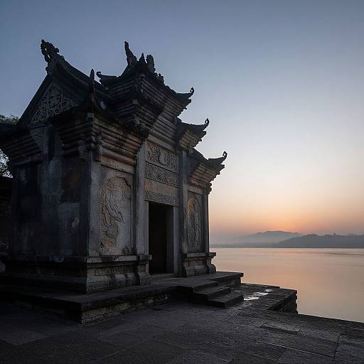 Photograph of an ancient, intricately carved stone temple with ornate roof details, silhouetted against a serene, twilight sky over a calm