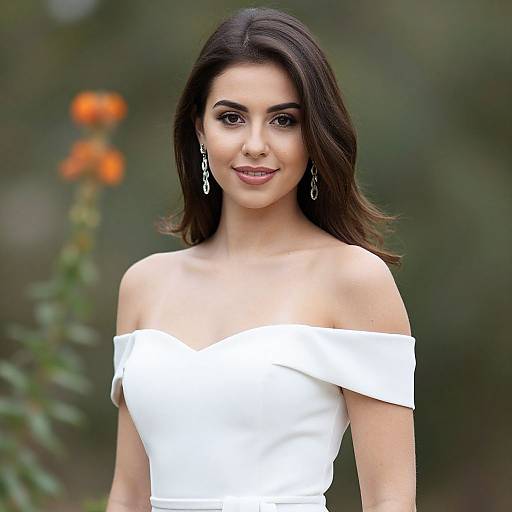 Photograph of a smiling young woman with dark brown hair, wearing an off-the-shoulder white dress and dangling earrings, against a blurred green and