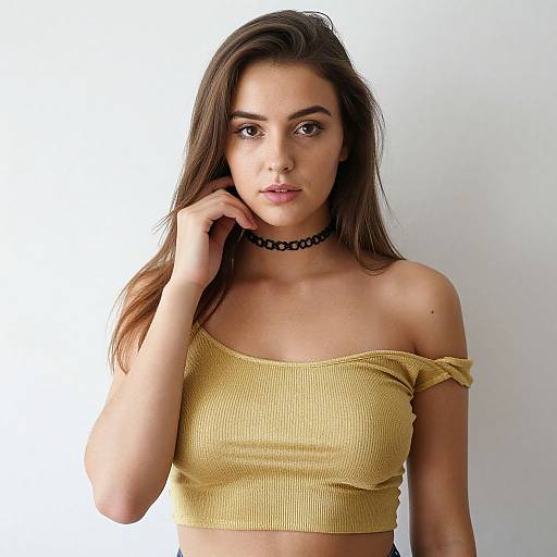 Photograph of a young woman with long brown hair, wearing a yellow off-shoulder crop top and black choker, against a plain white background