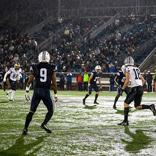 Photograph of a rainy night football game; two players in black and white uniforms, numbers 9 and 25, on a wet field with a