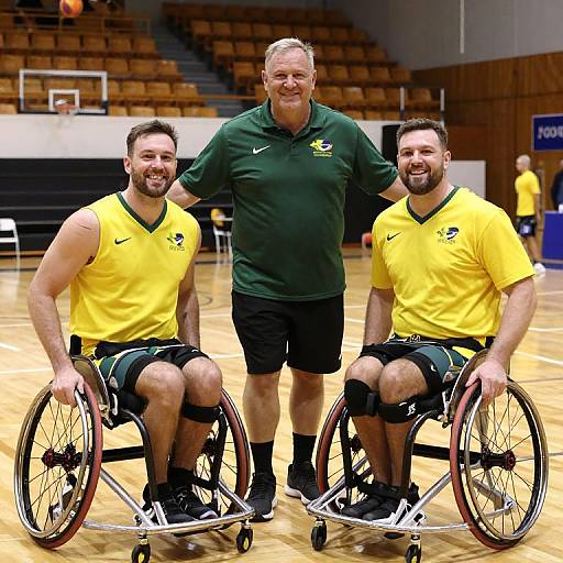 Photograph of two smiling, bearded men in yellow sports shirts and black shorts, in wheelchairs, standing with a smiling man in a green