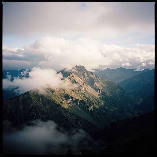 Photograph of a mountain range with sunlight breaking through clouds, casting dramatic shadows on rugged peaks and green valleys below.