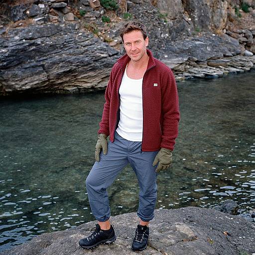 Photograph of a smiling middle-aged man with short brown hair, wearing a red fleece, white tank top, gray pants, green gloves, and black