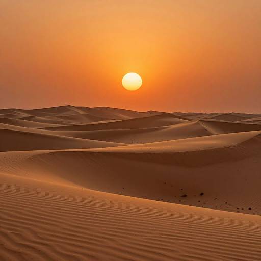 Photograph of a serene desert sunset with an orange sun, rippling sand dunes in the foreground, and a gradient sky from orange to yellow.