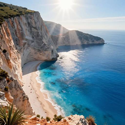 Photograph of sunlit coastal cliffs with sandy beach, turquoise water, and clear blue sky; sun rays shining over rugged cliffs.