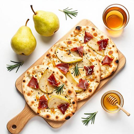 Photograph of pears, honey, flatbreads with caramelized onions, and rosemary on a wooden board, accompanied by two honey-filled glasses