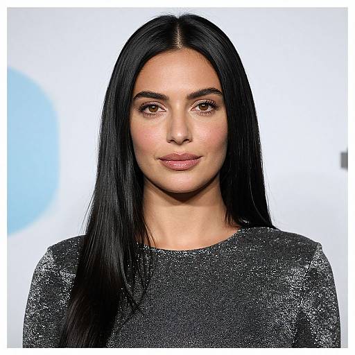 Photograph of a woman with long, straight black hair, wearing a glittery black top, smiling subtly against a white background.