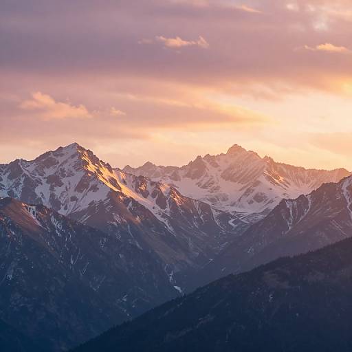 Photograph of a snow-capped mountain range at sunset, with purple and pink clouds in the sky, casting warm golden light on the peaks, and