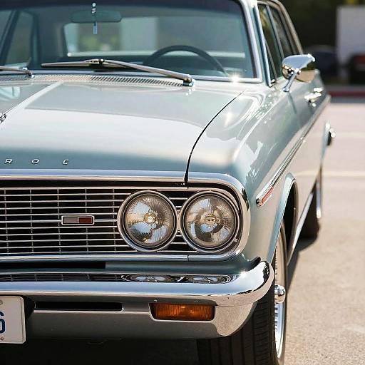 Photograph of a classic silver 1970s car with dual round headlights, chrome grille, and license plate, parked on a sunlit street.