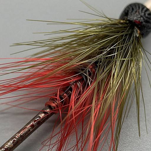 Close-up photograph of a brush with metallic handle, featuring gold and red synthetic bristles, showcasing detailed texture and color contrast.