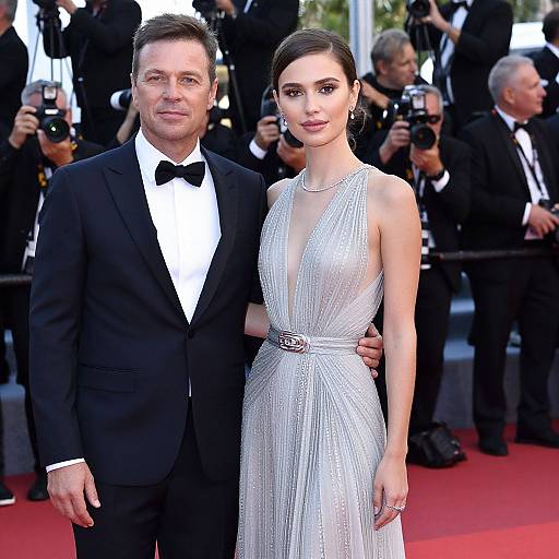 Photograph of George Clooney in a black tuxedo and Amal Clooney in a sparkling, sleeveless white gown at a red carpet event