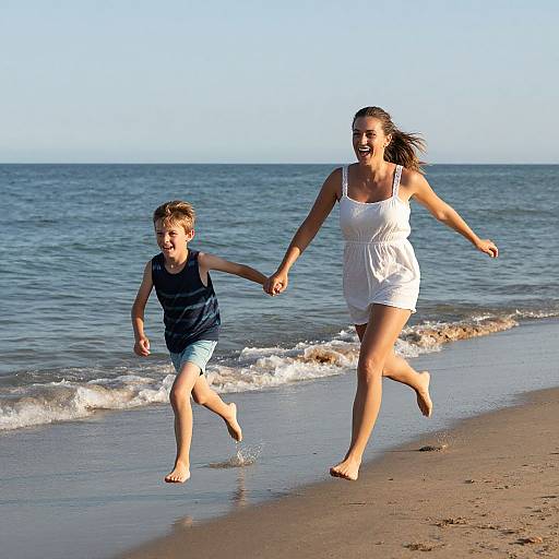 Photograph of a smiling woman in a white dress and a young boy in a navy tank top and blue shorts, holding hands and running barefoot along