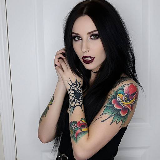 Photograph of a pale-skinned woman with long black hair, dark makeup, and tattoos, including a spider web and colorful flower on her arm,