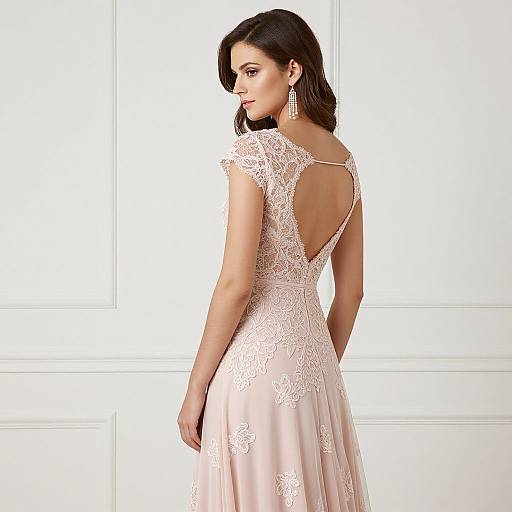 Photograph of a brunette woman with medium skin tone, wearing a pink lace-back, short-sleeve wedding dress, looking over her shoulder, against