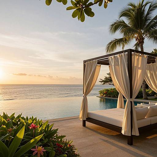 Sunset over ocean, four-poster bed with white curtains, tropical palm tree, and lush greenery in foreground. Photograph.