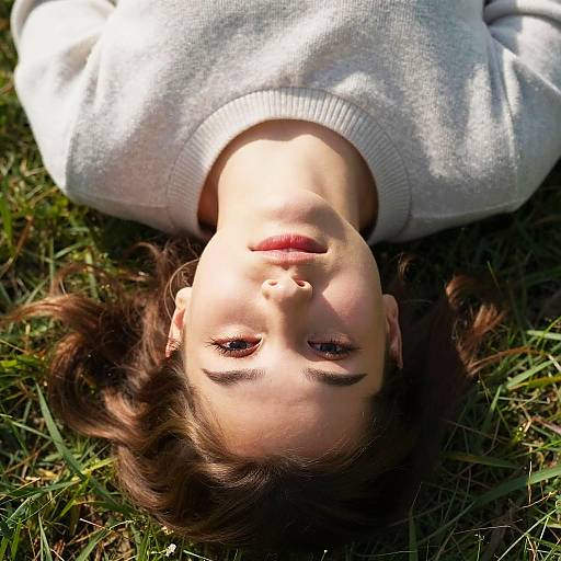 Photograph of a young girl with light brown hair and fair skin, lying on grass, wearing a white sweater, sunlight highlighting her face.