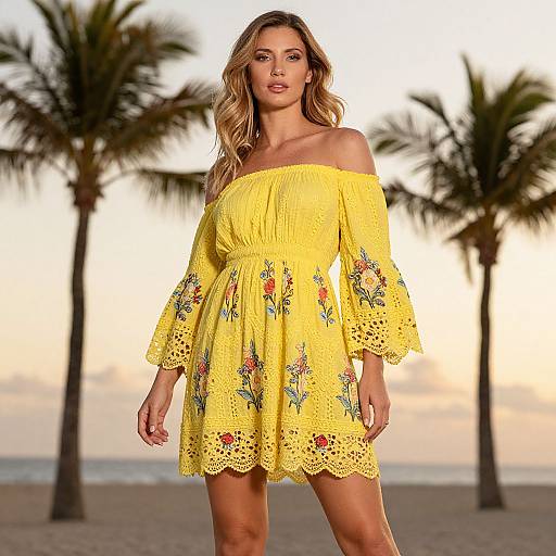 Photograph of a blonde woman in a yellow off-shoulder floral dress standing on a beach with palm trees and a sunset.