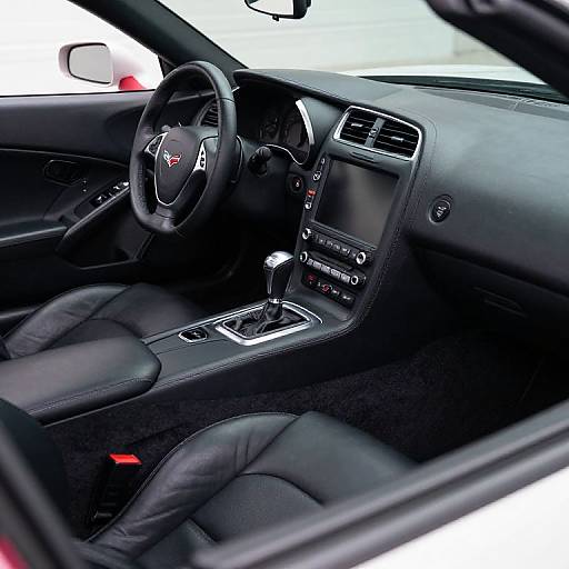 Photograph of a modern car interior with black leather seats, Acura emblem on steering wheel, gear shift, center console controls, and red seatbel