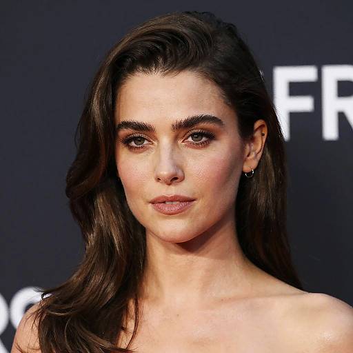Photograph of a woman with long, dark brown hair, fair skin, and brown eyes, wearing subtle makeup and small earrings, against a black background