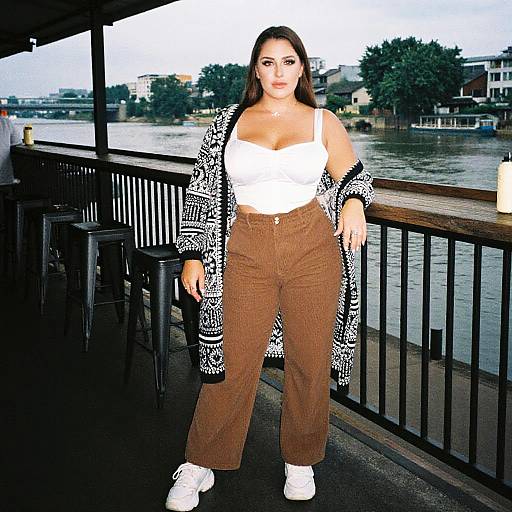 Photograph of a curvy woman with long brown hair, wearing a white crop top, brown high-waisted pants, and white sneakers, standing