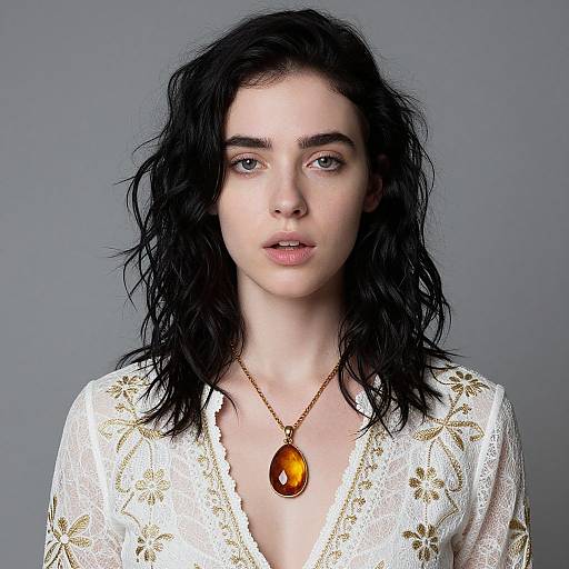 Photograph of a pale-skinned woman with wavy black hair, wearing a white lace blouse with gold floral patterns, and a gold necklace with an