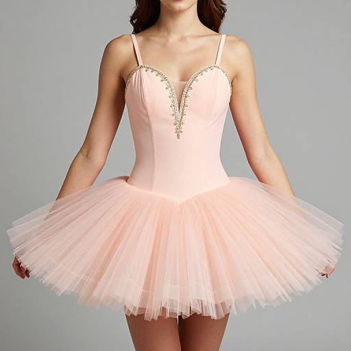 Photograph of a slender woman wearing a pink, strapless, sweetheart-neck, tulle ballerina dress with delicate gold trim, against a plain