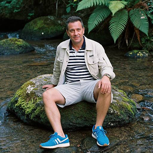 Photograph of a middle-aged man with short dark hair, wearing a white jacket, black and white striped shirt, white shorts, and blue sneakers,