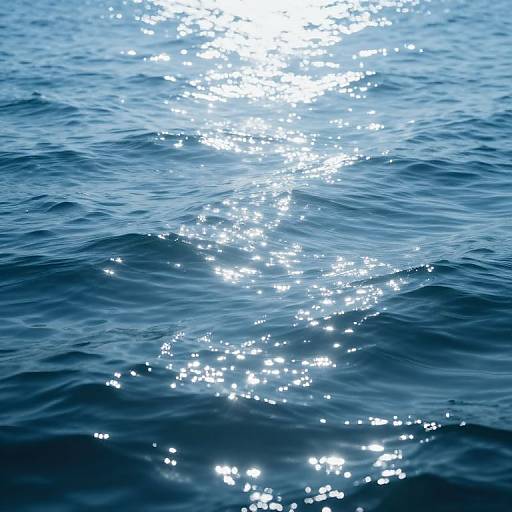 Photograph of sparkling blue ocean water with sunlight reflecting off gentle waves, creating a shimmering, bright white path through the water.