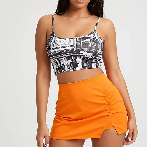 Photograph of a woman with long dark hair wearing a black-and-white patterned crop top and bright orange high-waisted mini skirt.