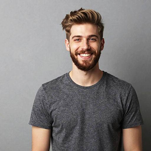 Photograph of a smiling, bearded young man with light brown hair, wearing a dark gray, short-sleeved, crew-neck t-shirt,