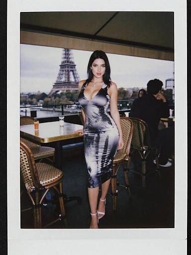 Photograph of a confident woman with long black hair, wearing a silver, form-fitting, deep V-neck dress, standing in a Paris café with
