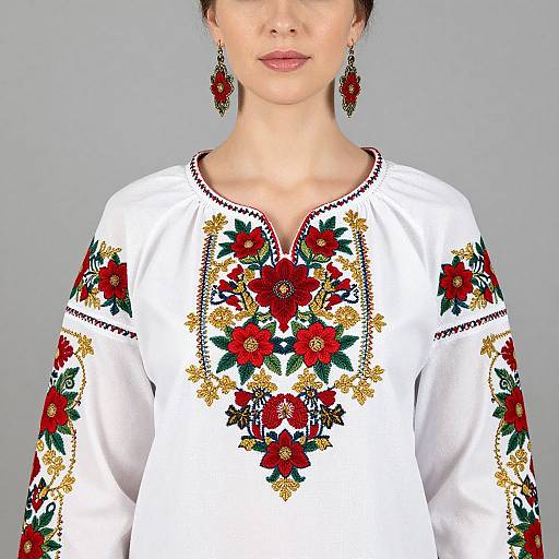 Photograph of a woman in a white, long-sleeved, embroidered blouse with red, green, and gold floral patterns, wearing matching red and