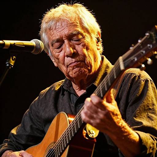Photograph of an elderly man with white hair and wrinkled face, passionately playing an acoustic guitar on stage, illuminated by stage lights.
