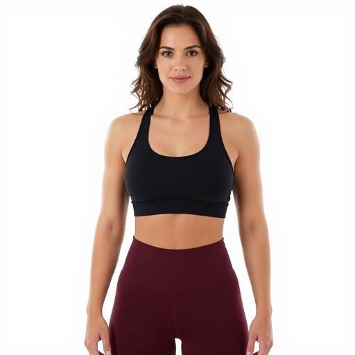Photograph of a fit, attractive woman with wavy brown hair, wearing a black sports bra and maroon leggings, standing against a white background.